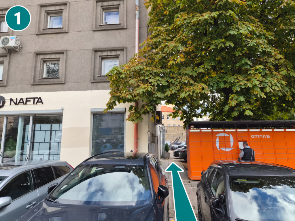 Praėjimas tarp pastato ir Omniva paštomato, pažymėtas rodykle.